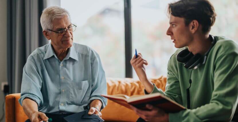 Young man sits with an older man on a couch in a discussion.